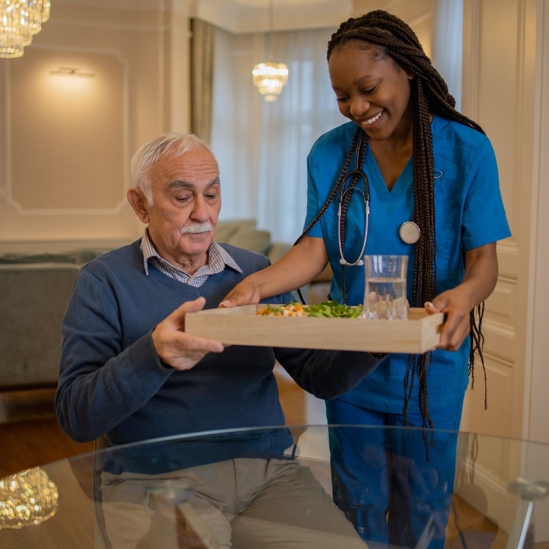 Caregiver serving a meal to an elderly resident in an elegant dining room
